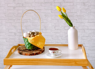 A basket with eggs, a cup of tea, and a vase of yellow tulip on the coffee table against the wall in the loft style. Concept of a feeling of coziness at home.