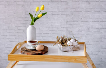 A box with eggs, a cup of tea, and a vase of yellow tulip on the coffee table against the wall in the loft style. Good morning. Concept of a feeling of coziness at home.