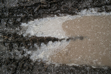 Wheel tracks on the soil. Tire tracks on the ground. Soil texture background. Ground. Soil closeup and high detail. Ground surface. Late fall. Autumn. Frozen Puddle. Ice and Snow