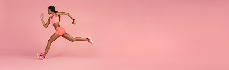 Sportswoman sprinting on a large pink background