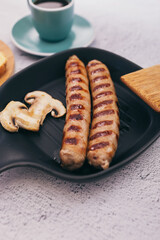 Hot juicy sausages in a frying pan with mushrooms, bread and sauce. On a stone background, top view.