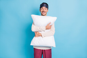 Portrait of nice cheerful funny guy wearing sleep clothes embracing soft pillow isolated over bright blue color background