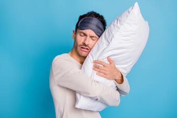 Portrait of nice sad worried guy embracing lying on soft pillow seeing bad dreams isolated over bright blue color background
