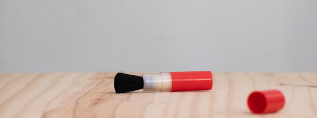 Black bristled lens cleaning brush with red color clip on a wooden table lay flat.