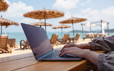 Closeup of a woman working and typing on laptop tcomputer on the beach