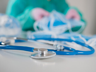 Close-up of a stethoscope lying on a doctor's table against the background of a doctor counting medical masks.