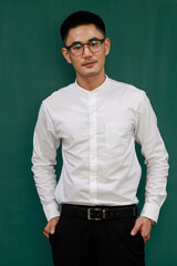 Portrait of young and handsome Asian man wearing eyeglasses and casual business clothes, white shirt and black trousers, standing pose with self-confidence with green background and copy space