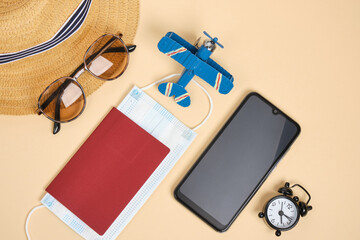 passport hat sun glasses alarm clock and toy plane on beige background Top view flat lay corona virus protection