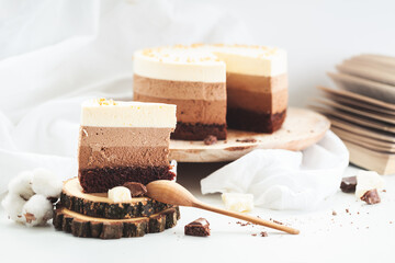 Three layered chocolate mousse cake on the wooden stand on white background. Good morning with fresh coffee and chocolate souffle cake. Vintage background