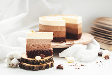 Three layered chocolate mousse cake on the wooden stand on white background. Good morning with fresh coffee and chocolate souffle cake. Vintage background