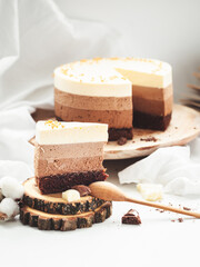 Three layered chocolate mousse cake on the wooden stand on white background. Good morning with fresh coffee and chocolate souffle cake. Vintage background