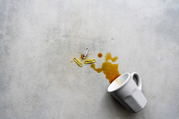 Eine umgekippte Kaffeetasse und bunte Büroklammern auf einem grauen Schreibtisch. Flat lay,...