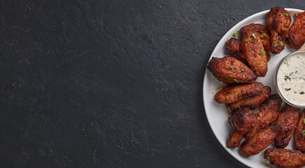 Grilled chicken wings with sauce on black stone background with copy space. Top view, flat lay 