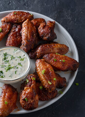 Grilled chicken wings with sauce on black stone background.