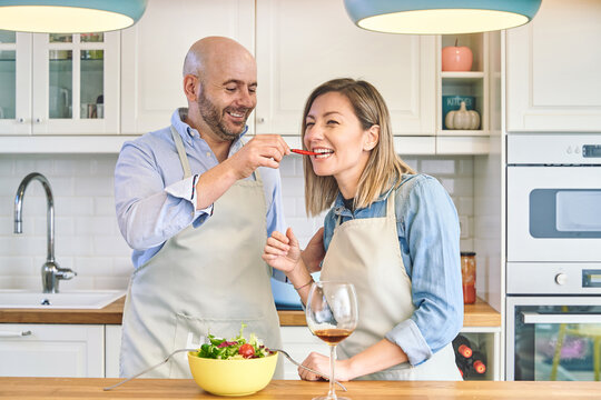 Happy couple cooking at home. He offers her a chili pepper. Family kitchen concept. 