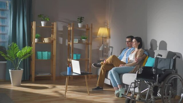 a couple of spouses a young disabled woman in a wheelchair spend time together sitting on the couch