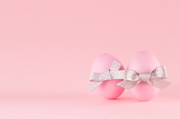 Exquisite soft pink easter eggs with silver bow standing on pastel pink background.