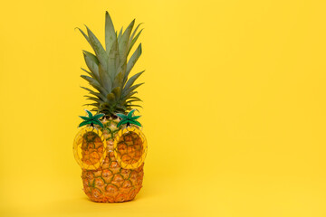 Pineapple with funny pineapple glasses on a yellow background with copy space