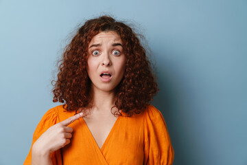 Shocked redhead curly girl pointing finger at herself