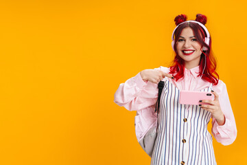 Joyful girl with red hair in headphones pointing finger at her cellphone