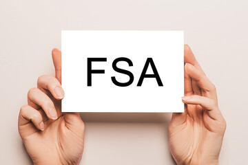 Female hands hold card paper with text FSA on a yellow background. Business and finance concept