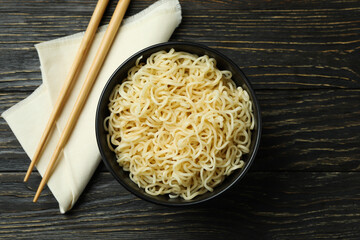 Napkin with chopsticks and bowl with noodles on wooden background