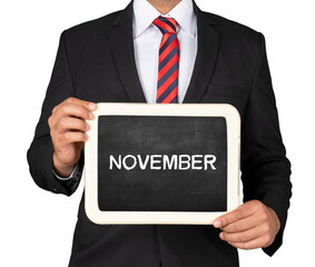  A Businessman holding slate mini blackboard with message November