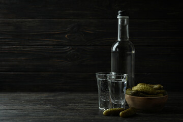 Bottle and shots of vodka, and pickles on wooden background