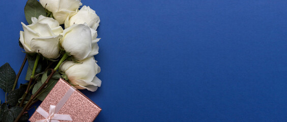 Postcard. White roses on a blue background with a pink gift box. Congratulations on March 8, Valentine's Day, Mother's Day, Birthday, Anniversary, Easter, Wedding, Teacher's Day, to women. Banner.