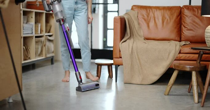 Young housewife vacuuming floor with cordless vacuum cleaner, feels satisfied with a comfortable home appliances. Comfortable home life with modern and smart appliances