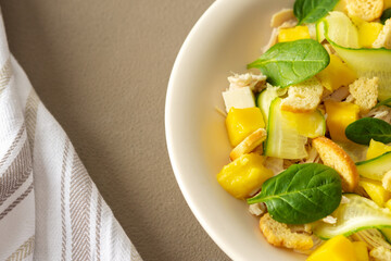 Plate with salad close-up on a brown background, salad of cucumber and chicken breast, mozzarella and croutons with sweet mango pieces and spinach
