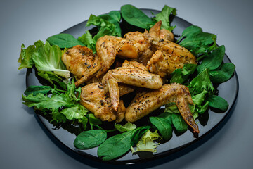 Chicken wings with greens and salad on a black plate on a blue background