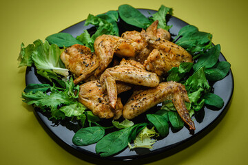 Chicken wings with greens and salad on a black plate on a yellow background