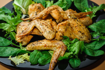 On a black plate chicken wings with herbs and salad on an orange background