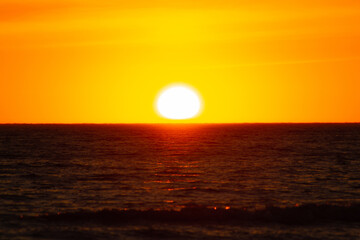 Orange sunset over the horizon turning  red cloudy sky with beautiful sea foreground