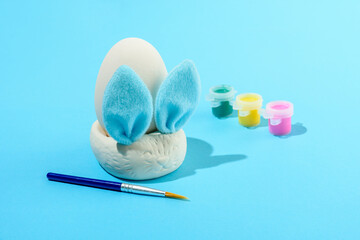Easter egg painting set with bunny. Brush and paints on light blue background
