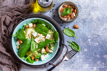 Couscous salad with pear, spinach, almonds, feta cheese and vinaigrette sauce on a gray stone table. Top view flat lay. Copy space.