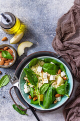 Couscous salad with pear, spinach, almonds, feta cheese and vinaigrette sauce on a gray stone table. Top view flat lay. Copy space.