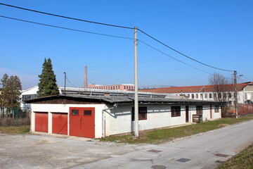 Elongated white garage and storage building in old industrial part of town surrounded with cracked paved street and factory buildings in background on warm sunny winter day