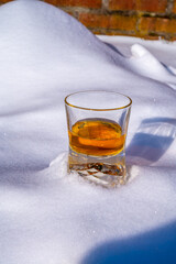 Glass of cold scotch single malt whisky on white snow