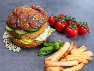 Tasty vegetarian vegan lunch with hamburger made from vegetables based burger, organic bun with seeds and fresh vegetables and french fried potatoes