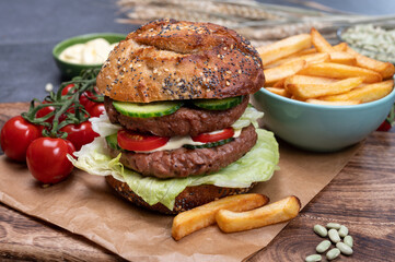 Tasty vegetarian vegan lunch with double decker hamburger made from plant based soya beans burger, organic bun with seeds and fresh vegetables and french fried potatoes
