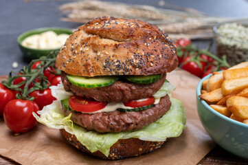 Tasty vegetarian vegan lunch with double decker hamburger made from plant based soya beans burger, organic bun with seeds and fresh vegetables and french fried potatoes