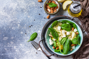 Couscous salad with pear, spinach, almonds, feta cheese and vinaigrette sauce on a gray stone...
