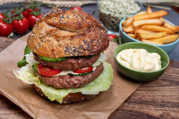 Tasty vegetarian vegan lunch with double decker hamburger made from plant based soya beans burger, organic bun with seeds and fresh vegetables and french fried potatoes