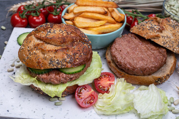 Tasty vegetarian vegan lunch with hamburger made from plant based soya beans burger, organic bun with seeds and fresh vegetables and french fried potatoes