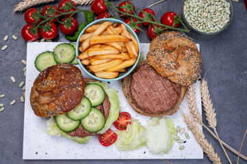 Tasty vegetarian vegan lunch with hamburger made from plant based soya beans burger, organic bun with seeds and fresh vegetables and french fried potatoes