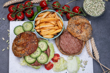 Tasty vegetarian vegan lunch with hamburger made from plant based soya beans burger, organic bun with seeds and fresh vegetables and french fried potatoes