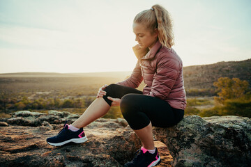 Caucasian female hiking on mountain injured leg holding knee sitting on rock waiting for help