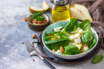 Couscous salad with pear, spinach, almonds, feta cheese and vinaigrette sauce on a gray stone table. Copy space.
